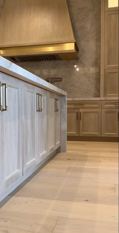 an empty kitchen with white cabinets and wood flooring, in the middle of a large room