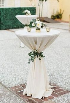 a white table topped with flowers and greenery sitting on top of a brick floor