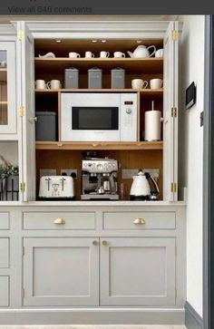 a kitchen with lots of white cabinets and appliances on it's shelves, along with an open microwave oven