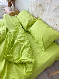 an unmade bed with lime green sheets and pillows on the floor next to a window