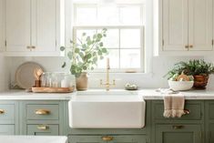 a kitchen with green cabinets and white counter tops, gold pulls on the cabinet doors