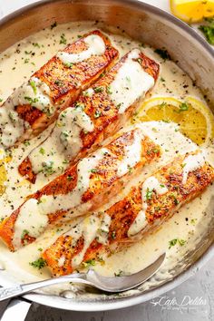 two salmon fillets in a creamy sauce with lemon wedges