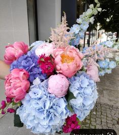 a bouquet of pink, blue and purple flowers in front of a building on the sidewalk