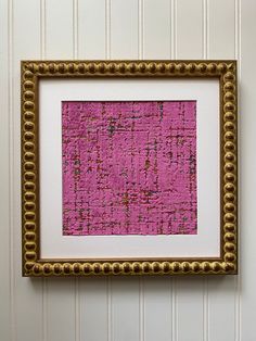 a pink and gold framed artwork hanging on a wall next to a white striped wall