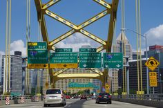 two cars driving over a bridge with tall buildings in the background