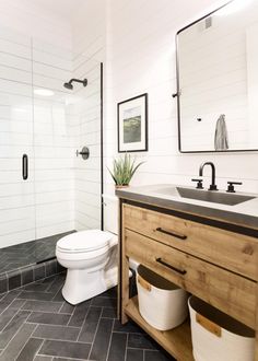 a white toilet sitting next to a walk in shower under a bathroom mirror above a sink