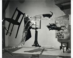 black and white photograph of two cats jumping into water from a fountain in front of a chair