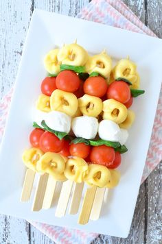 a white plate topped with tomatoes and cheese skewers on top of a wooden table