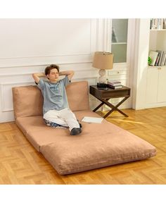 a man sitting on top of a futon bed in a living room next to a lamp