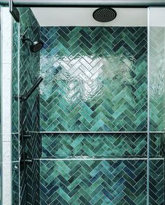 a shower with green tiles and a black faucet in the shower head is shown