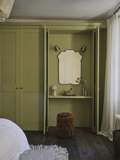 a bedroom with green painted walls and wooden flooring, an armoire has a mirror on it