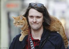 a man walking down the street with a cat on his shoulders