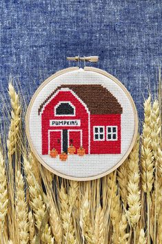 a red house with pumpkins in front of it and some ears of wheat behind it