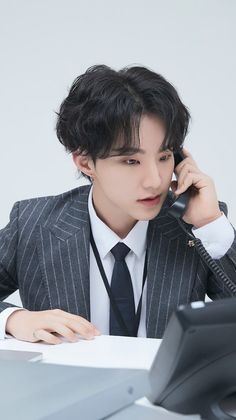 a man in a suit talking on a phone while sitting at a desk with a computer