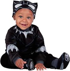 a baby dressed in a batman costume sitting on the floor with his feet crossed and smiling