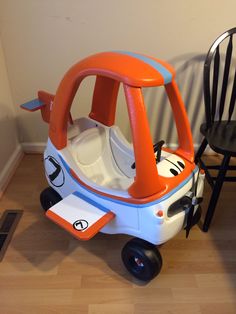 an orange and white toy car sitting on top of a hard wood floor next to a black chair