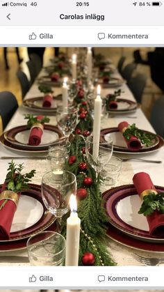 the table is set for christmas dinner with candles and greenery on it, along with other place settings