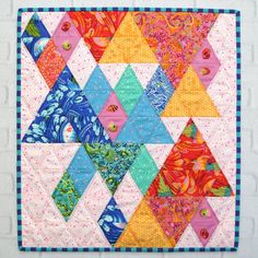 a quilted wall hanging on the side of a white brick wall with colorful triangles