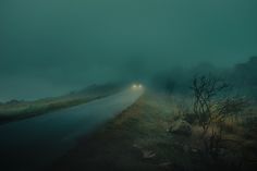 a car driving down a foggy road at night with the headlights turned on in the distance