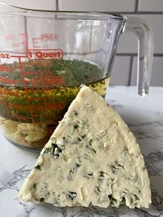 a wedge of cheese sitting next to a measuring cup on top of a marble counter