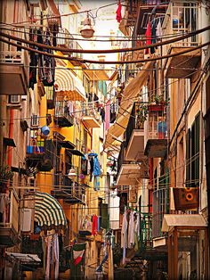 an alleyway with clothes hanging from the balconies and umbrellas above it