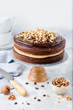 a chocolate cake sitting on top of a wooden stand next to a bowl of nuts