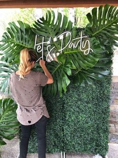 a woman standing next to a lush green wall with the words let's party written on it