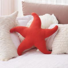 a red starfish pillow sitting on top of a bed next to two white pillows