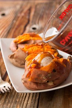 a plate with baked potatoes and cheese being drizzled over them on a wooden table