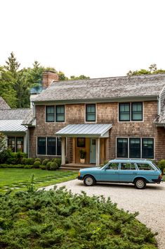 a blue car is parked in front of a large brown house with trees and bushes