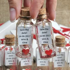 two tiny bottles with hearts in them are being held by someone's hand and the bottle is labeled save the date