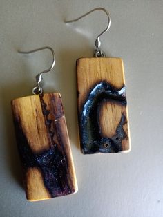 two square wooden earrings with metal hooks on white surface, one has blue and the other is brown