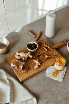 a wooden cutting board topped with lots of food on top of a table next to jars