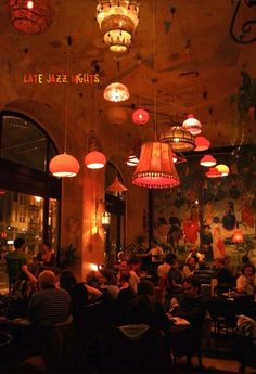 people sitting at tables in a restaurant with chandeliers hanging from the ceiling