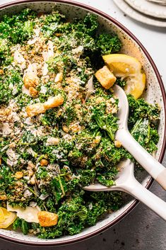 a bowl filled with broccoli covered in cheese and lemon wedges next to silverware