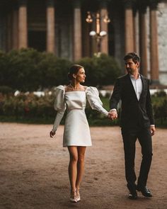 a man and woman holding hands while walking in front of a large building with columns