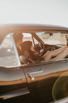 a man and woman sitting in the driver's seat of a black sports car