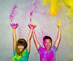 two people with their arms in the air while they have colored powder on their hands