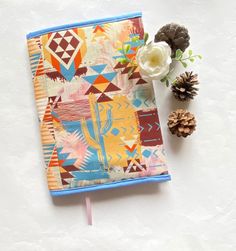 an open notebook sitting on top of a table next to a pine cone and flower