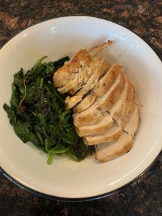 a white bowl filled with meat and greens on top of a granite countertop next to a wooden table