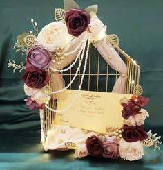 a wedding card in a cage with flowers and pearls on the sides, sitting on a green background