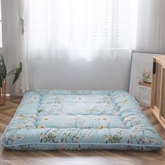 a blue mattress sitting on top of a wooden floor next to a window with white curtains