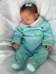 a baby sleeping in a blue outfit on top of a white blanket with a bow