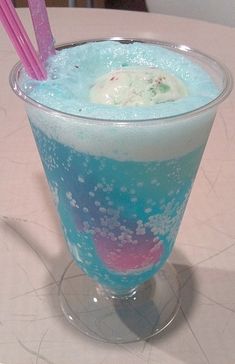 a blue drink with ice and straws in it sitting on a white table top