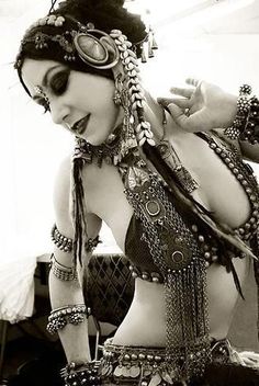 a woman in a belly ring and headdress poses for the camera with her hands on her hips