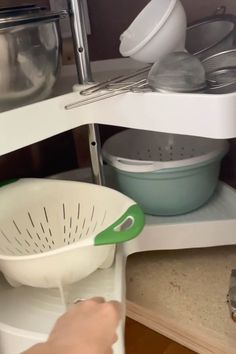 a person is holding a strainer in the corner of a kitchen cabinet with dishes on it