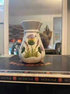 a vase sitting on top of a table in front of a mirror with flowers painted on it