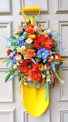 a yellow bucket with flowers in it hanging on the side of a white garage door