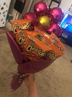 a hand holding a bouquet of chocolates wrapped in foil and balloons on the floor