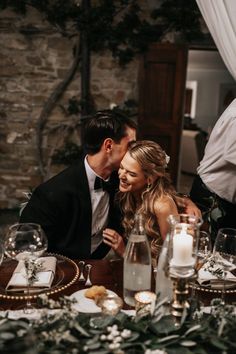 a man and woman sitting at a table with candles in front of them, one kissing the other